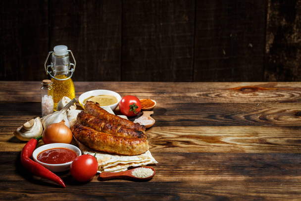 Grilled sausages, fresh vegetables, ingredients and spices on a wooden table - Photo, image