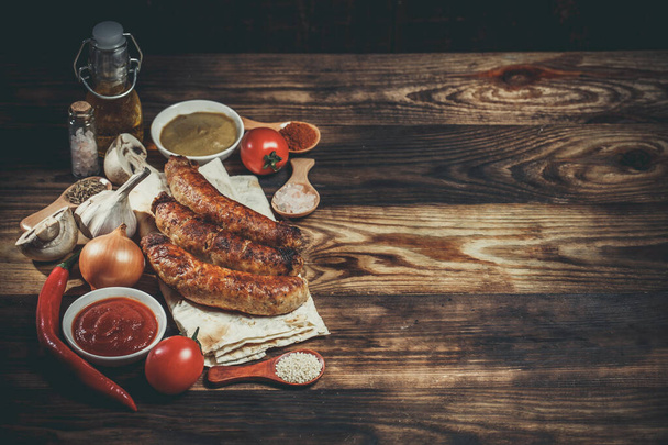 Grilled sausages, fresh vegetables, ingredients and spices on a wooden table - Fotoğraf, Görsel