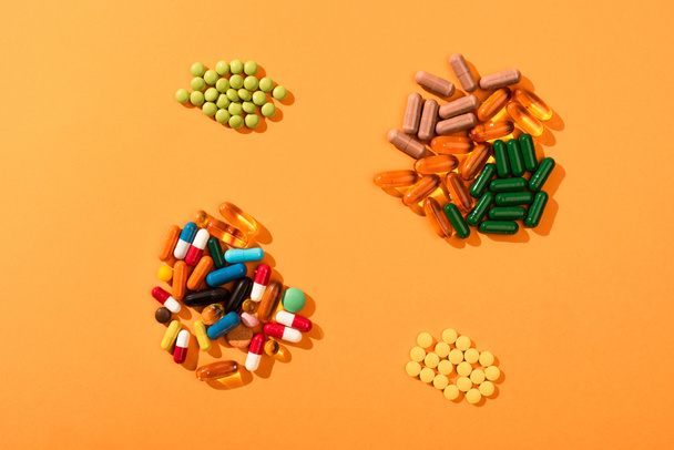 Bovenaanzicht van veelkleurige pillen en capsules op oranje achtergrond - Foto, afbeelding