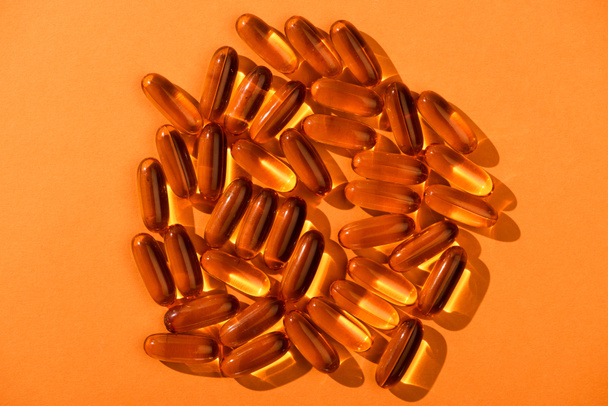 Bovenaanzicht van bruine visolie capsules op oranje achtergrond - Foto, afbeelding