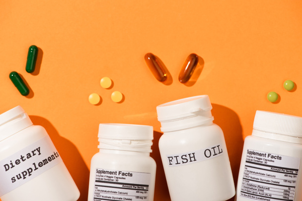 Ansicht von Containern mit Fischöl und Nahrungsergänzungsmitteln in der Nähe von Pillen auf orangefarbenem Hintergrund - Foto, Bild