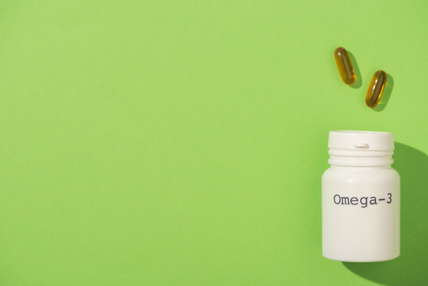Horní pohled na nádobu s nápisem omega-3 v blízkosti tobolek na zelené - Fotografie, Obrázek