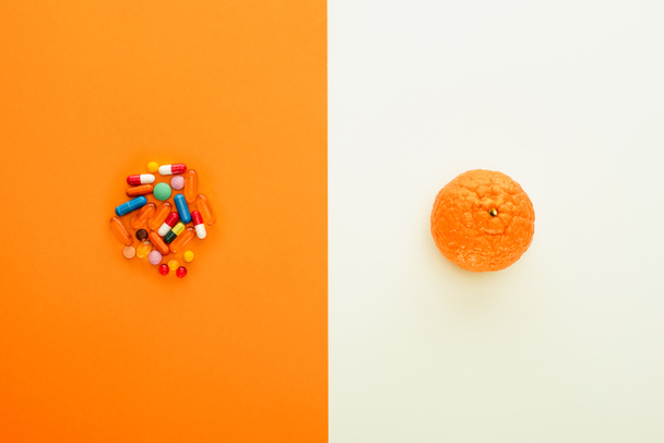 Bovenaanzicht van kleurrijke pillen en mandarijn op witte en oranje achtergrond - Foto, afbeelding