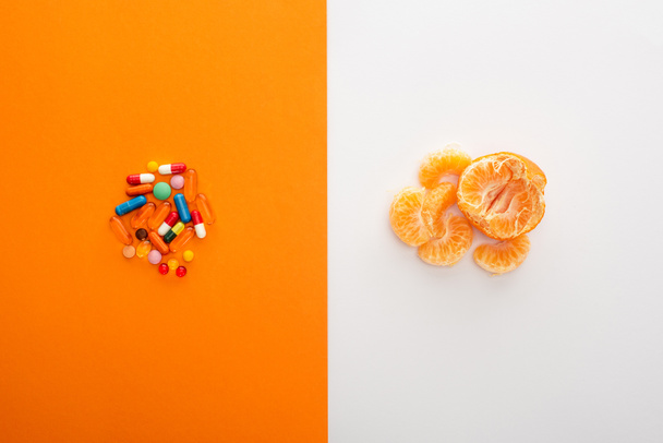 Top view of colorful medicines and mandarin on white and orange background - Photo, Image