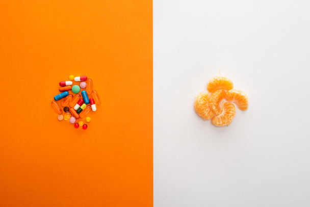 Draufsicht auf bunte Pillen und Mandarine auf Weiß und Orange  - Foto, Bild