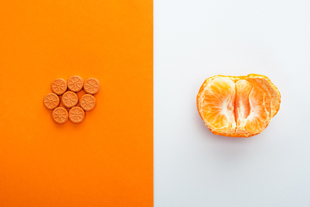 Top view of pills and mandarin half on white and orange background - Photo, Image