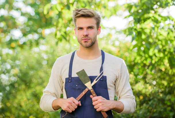Grilling food. Barbecue utensils. Cooking burgers. Man hold barbeque equipment. Summer weekend. Tools for roasting meat outdoors. Barbeque party. Picnic concept. Bbq chef. Handsome guy cooking food - Foto, imagen