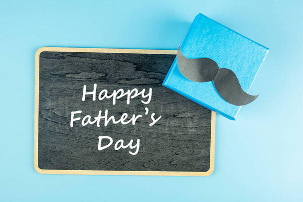 caja de regalo con bigote sobre fondo azul, preparación para el padre. Día Internacional del Hombre y Concepto del Día del Padre - Foto, imagen