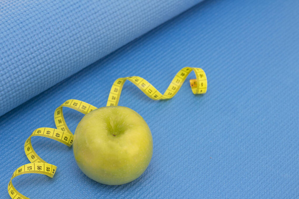 green apple, measuring tape on a sports mat of blue color. preparation for the summer season and the beach, weight loss and sports concept - Zdjęcie, obraz