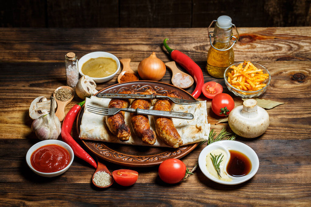 Grilled sausages, fresh vegetables, ingredients and spices on a wooden table - Fotó, kép