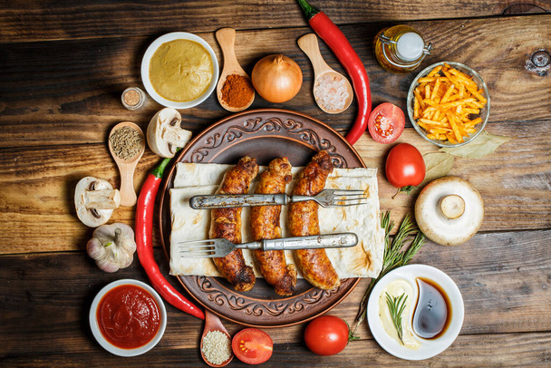 Grilled sausages, fresh vegetables, ingredients and spices on a wooden table - Foto, Bild