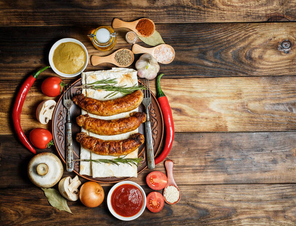 Grilled sausages, fresh vegetables, ingredients and spices on a wooden table - Fotografie, Obrázek