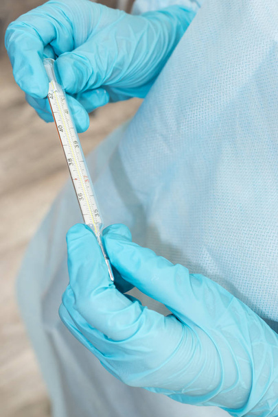 Руки медика в стерильных халатах и перчатках держат термометр
 - Фото, изображение