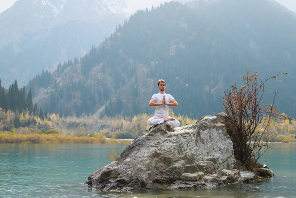 Un joven zen meditando. Yoga al aire libre en lago de montaña. Ejercicio Agni Stambhasana. - Foto, imagen
