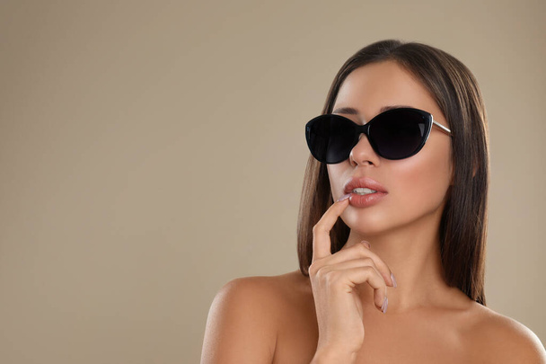 Beautiful young woman wearing sunglasses on beige background. Space for text - Photo, Image