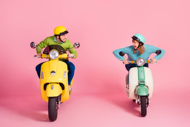 Who is first. Full length photo of crazy funny lady guy driving two vintage moped speed race competition wear casual outfit colorful protective headgear isolated pink color background - Photo, Image