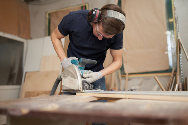 Worker in safety glasses and white gloves works on jigsaw in workshop . - Fotografie, Obrázek