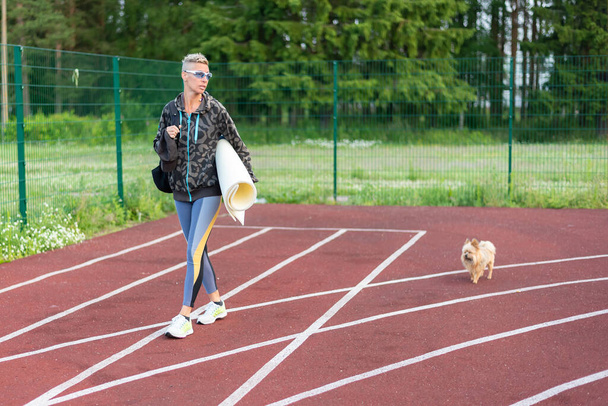 An adult woman trains at the stadium, along with a little dog. For any purpose. - Zdjęcie, obraz