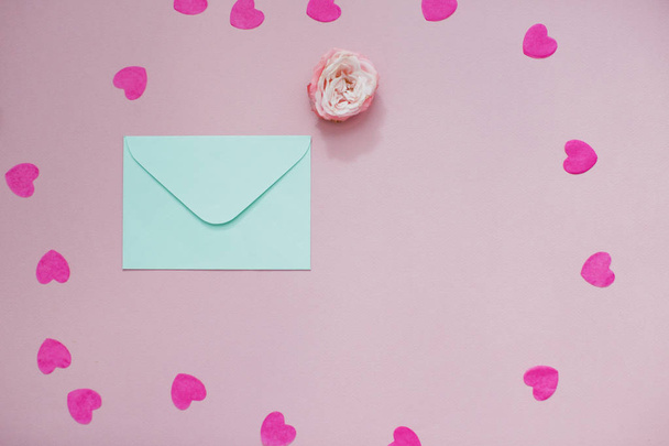 Mint envelope with a pink rose flower and heart shaped confetti. Flat lay, top view. - Foto, afbeelding