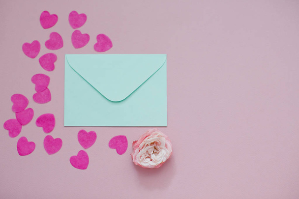 Mint envelope with a pink rose flower and heart shaped confetti. Flat lay, top view. - Foto, afbeelding