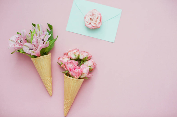 Jégkrém tölcsérek rózsaszín virágokkal és menta borítékkal rózsaszín pasztell háttérrel. Felülnézet - Fotó, kép