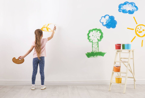 Little child painting on white wall indoors - Фото, изображение