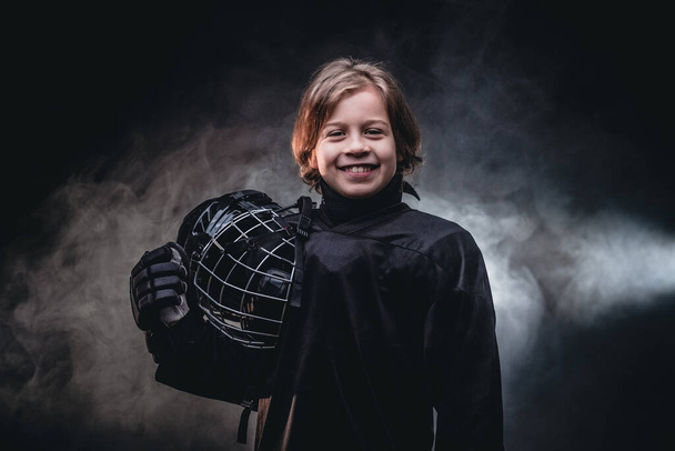 Giovane e gioioso giocatore di hockey in posa in uniforme da hockey nero per una foto in uno studio
 - Foto, immagini
