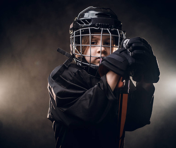 Joven jugador de hockey triste posando en uniforme para una foto en un estudio bajo los focos
 - Foto, Imagen