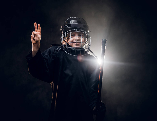 Young, 8-10 year old smiling hockey player posing in uniform for a photoshot in a dark studio under the spotlight - Fotografie, Obrázek