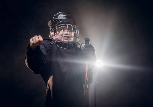 Young, 8-10 year old smiling hockey player posing in uniform for a photoshot in a dark studio under the spotlight - Foto, imagen