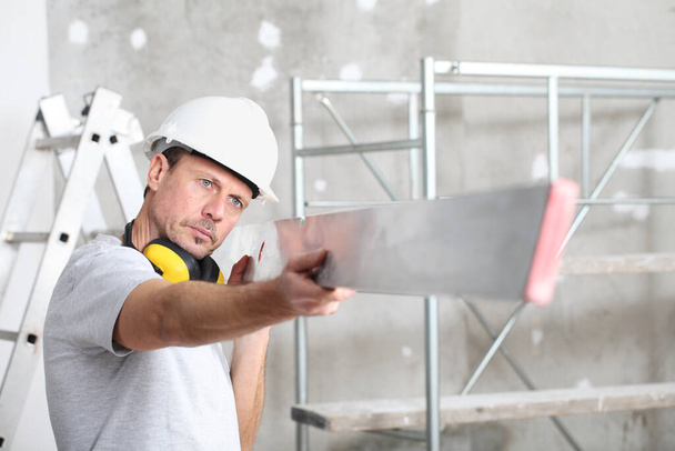 muž práce, zkontroluje rovinatý k vyrovnání stěny, s žebříkem a lešení v interiéru staveniště na pozadí - Fotografie, Obrázek