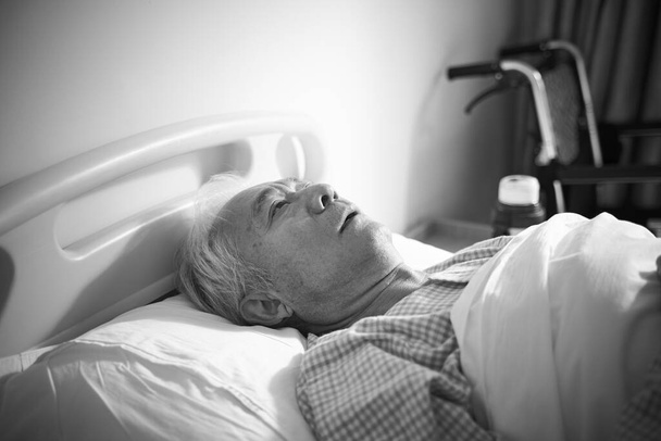 Hasta, yaşlı, Asyalı bir adam hastanede yatıyor. Üzgün ve çaresiz görünüyor. Siyah ve beyaz. - Fotoğraf, Görsel