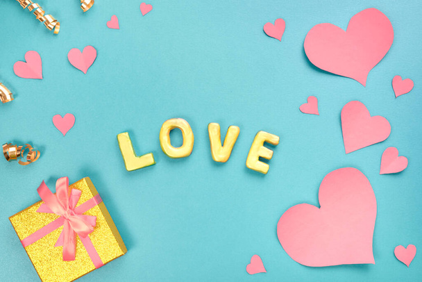 Valentines day concept. Pink paper hearts, gold gift, confetti and word love on blue background. Sweet holiday background. Top view, flat lay. - Photo, image