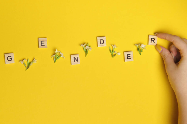 Word gender depicted by using wooden blocks and flowers on yellow bee background with woman hand pointing on it - 写真・画像