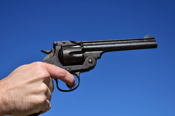Man holding a .44 or .45 caliber revolver outdoors with blue sky. - Фото, изображение