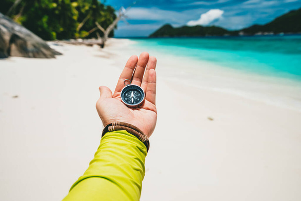 Male hand holding compass on tropical sandy beach and ocean. POV travel holiday adventure concept - Zdjęcie, obraz