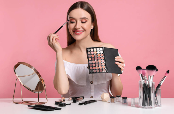 Beauty blogger applying eyeshadow on pink background - Foto, Bild
