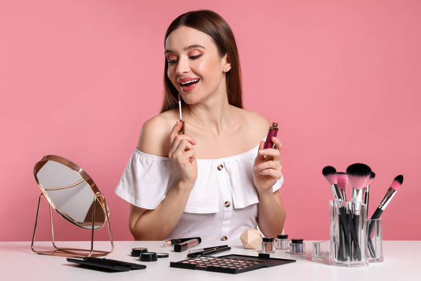 Beauty blogger applying lipgloss on pink background - Foto, imagen