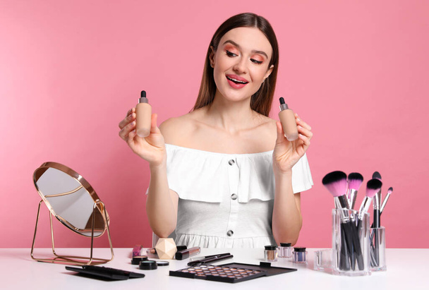 Beauty blogger showing bottles of foundation on pink background - Zdjęcie, obraz