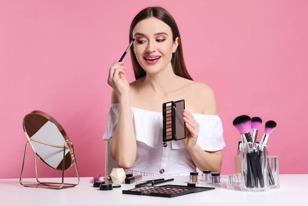Beauty blogger applying eyeshadow on pink background - Фото, изображение