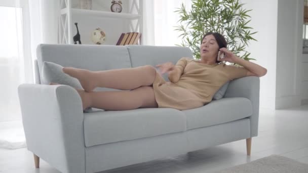 Elegant Caucasian senior woman standing up from couch with smartphone and leaving. Middle-aged stylish lady chatting at home on retirement. Active rich female retiree enjoying free life. Lifestyle. - Materiaali, video