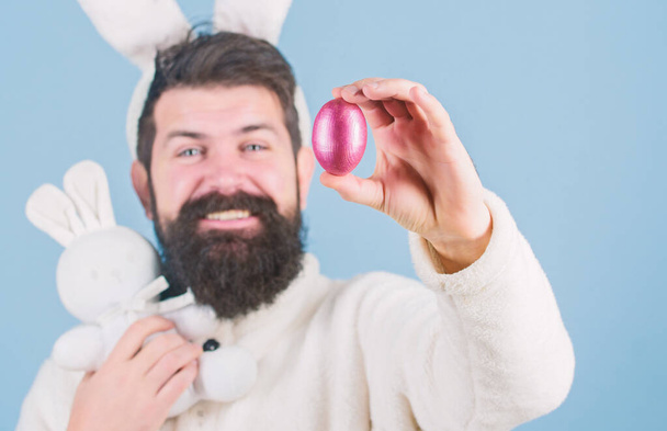 My precious. Bearded man wear silly bunny ears. Hipster cute bunny long ears blue background. Easter bunny. Having fun. Funny bunny with beard and mustache hold pink egg. Easter symbol concept - Фото, изображение