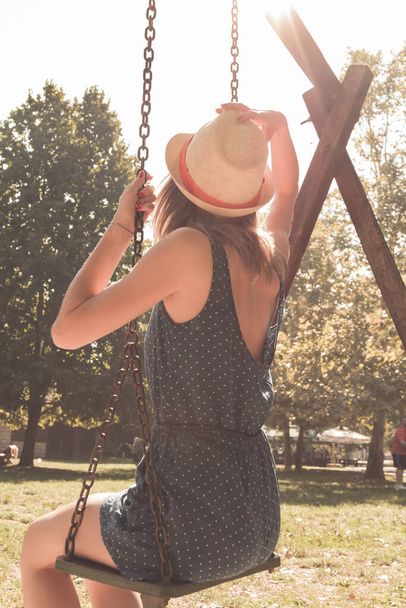 Cute young woman enjoying on a swing outdoors in summertime sunlight. - Photo, Image