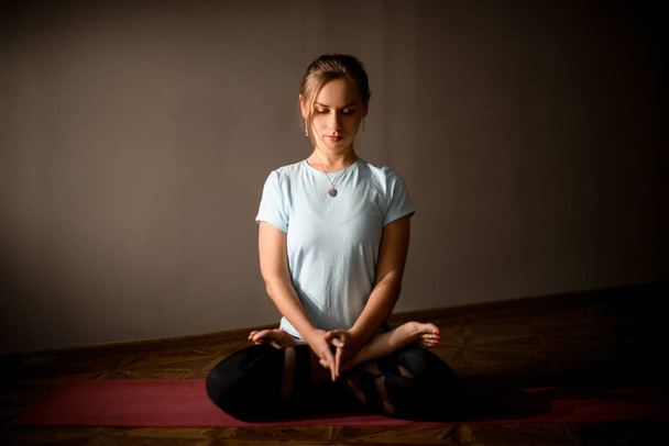 Girl in sport clothes practicing yoga in a studio room sitting in the lotus pose - Fotografie, Obrázek