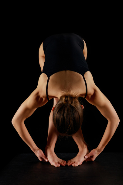 Çıplak ayaklı bir kız öne doğru eğilip siyah üzerine izole edilmiş egzersiz yapıyor.  - Fotoğraf, Görsel