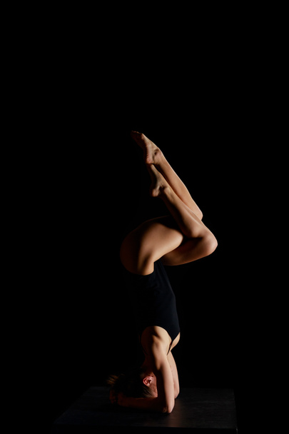 girl in bodysuit doing eagle legs handstand exercise isolated on black  - Photo, Image