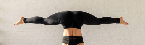 Panoramaaufnahme eines barfüßigen Mädchens beim breitbeinigen Handstand im Yoga-Studio  - Foto, Bild