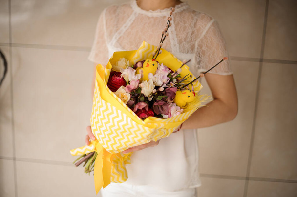 Woman holding a spring bouquet of different flowers decorated with willow branches, little chiken toy wrapped in yellow paper - Foto, Imagem