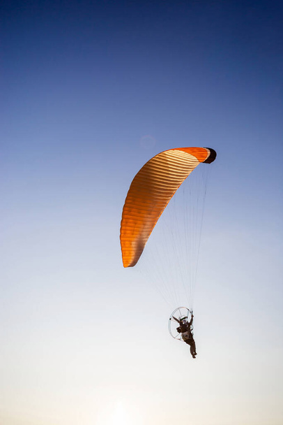 Paraglider flying in a deep blue sky. The sportsman flying on a paraglider orange color near the sea. - Photo, Image
