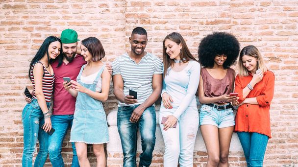 Glückliche multiethnische Freunde mit Smartphone im Hinterhof der Universität - Junge Leute in Suchtlaune mit Handy-Smartphone - Technologiekonzept mit immer vernetzten Millennials - Filterbild - Foto, Bild